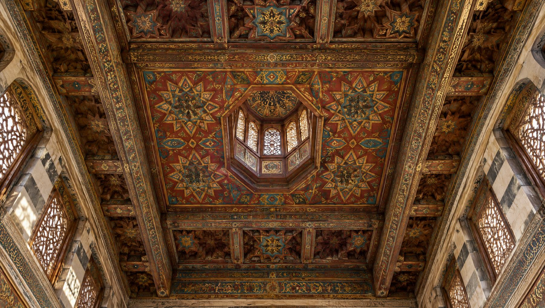 Looking up at a painted wooden ceiling with geometric stars in red, gold and turquoise