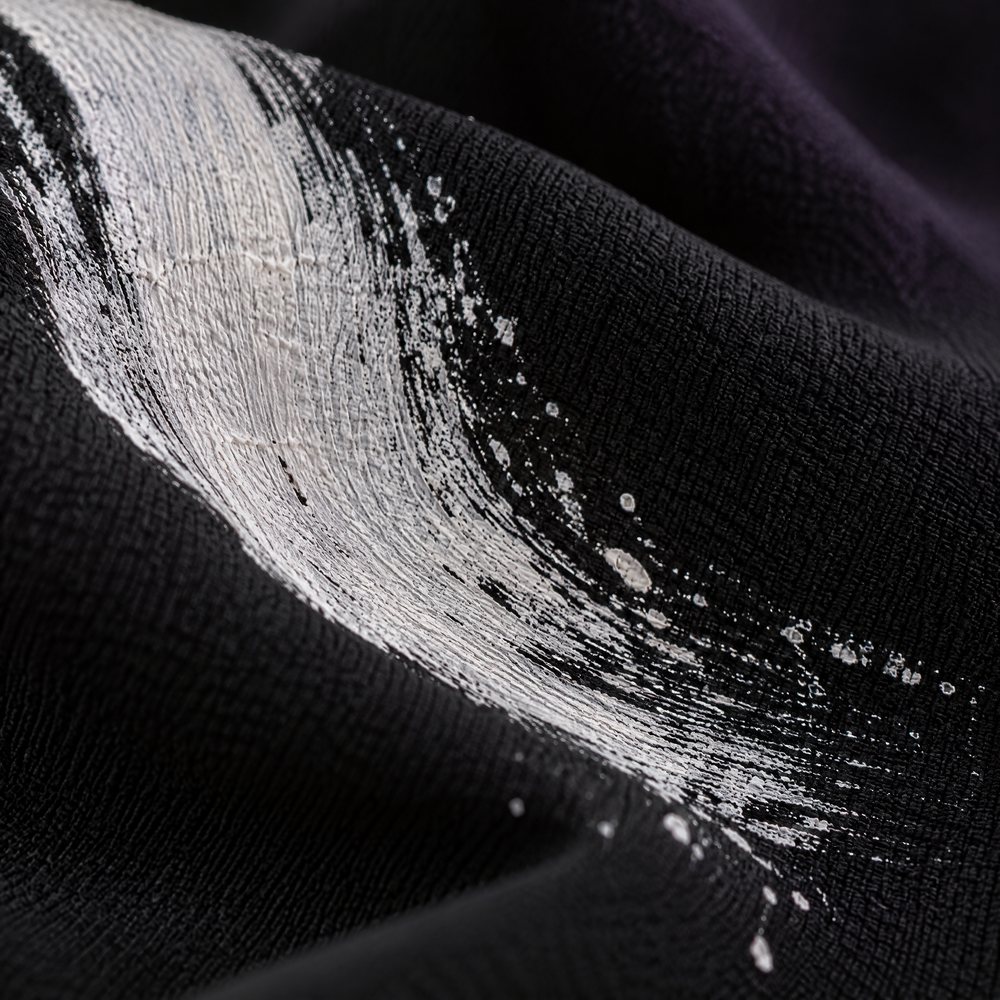 Close detail of the dry-brush edge of white paint on black crepe